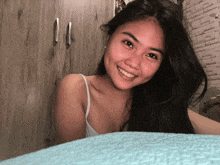 a woman in a white tank top smiles in front of a wooden cabinet