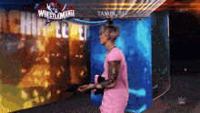 a man in a pink shirt stands in front of a sign that says wrestlemania