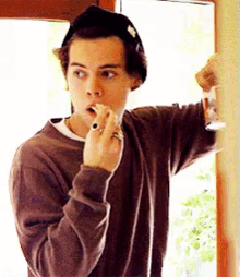 a young man wearing a brown sweater and a black hat is applying lipstick