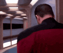 a man in a red jacket is standing in a hallway looking down