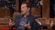 a man in a suit is talking into a microphone with benedict_fan written on the bottom