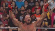 a shirtless wrestler stands in front of a crowd with the letters n on the bottom left