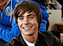 a young man wearing a leather jacket and a blue sweatshirt with the letter b on it