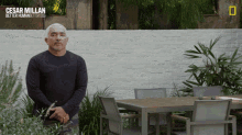 a man in a black shirt stands in front of a white brick wall with the words cesar millan better human better dogs