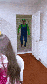 a man in overalls and a green hat is standing in a doorway
