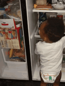 a baby in a diaper reaches into a fridge with a box of chicken noodle soup