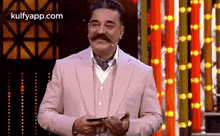 a man with a mustache is standing in front of a microphone holding a cell phone .