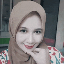 a woman wearing a hijab and a floral shirt smiles for the camera