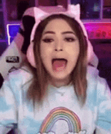 a girl wearing headphones and a cat ear headband is sitting in a chair with her mouth open .