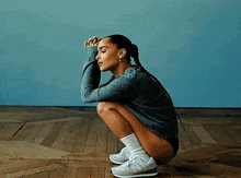 a woman is squatting down on a wooden floor wearing new balance sneakers