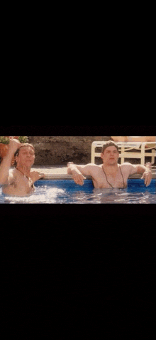 two men are standing in a swimming pool without shirts on .