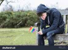 a young man is sitting on a bench with a rainbow flag