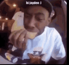 a man in a hat is eating a sandwich with the words hi jayden written on the bottom .