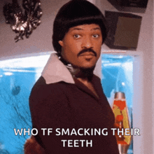 a man with a wig and mustache says who tf smacks their teeth