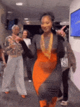 a woman in an orange dress is dancing in a hallway with other people