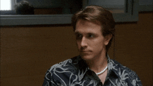 a man wearing a pearl necklace and a patterned shirt