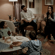 a man and woman sit on a couch while two children sit at a table with cookies
