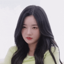 a close up of a woman with long black hair wearing a green shirt and making a funny face .