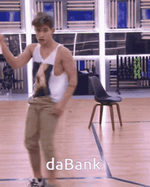 a man in a white tank top is dancing on a wooden floor with the word dabank behind him