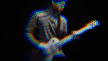 a man in a striped shirt is playing a guitar in the dark .