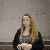 a young woman with curly hair is holding a cup of coffee .