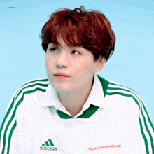 a young man with red hair is wearing a white shirt and a green adidas jacket .