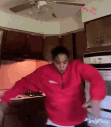 a man in a red sweatshirt is dancing in a kitchen with a ceiling fan and a sign that says baby hoop