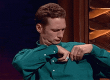 a man wearing a green shirt is adjusting his sleeves