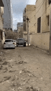 a black suv is parked on the side of a dirt road between two buildings .