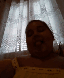 a woman is taking a selfie in front of a window with curtains .