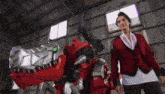a man in a red jacket is standing next to a large toy dinosaur in a warehouse .