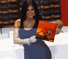 a woman in a blue dress is holding a picture in front of a fnac sign