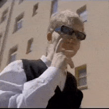 a man wearing sunglasses is smoking a cigarette while standing in front of a building .