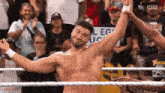 a shirtless wrestler in a wrestling ring with a crowd behind him and a sign that says college uc