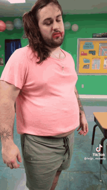 a man with long hair and a tattoo on his arm is wearing a pink shirt and green shorts