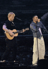 a man singing into a microphone while another man holds a guitar