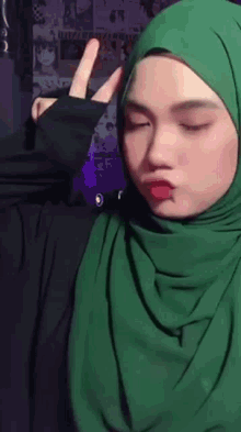 a woman in a green hijab is making a peace sign .