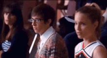 a man wearing glasses sits next to a woman wearing a cheerleader uniform