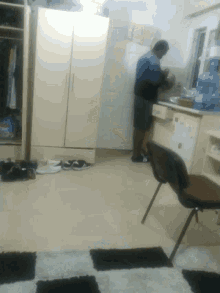 a man is standing in a room with a chair and a fridge