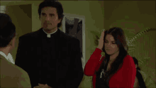 a woman in a red sweater stands in front of a priest