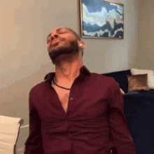 a man with a beard wearing a maroon shirt is standing in front of a couch .
