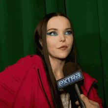 a woman wearing a red jacket is holding a microphone that says extra