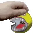 a hand is holding a tennis ball with a shark mouth .