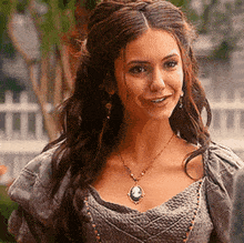 a woman wearing a necklace and earrings is smiling while standing in front of a white fence .