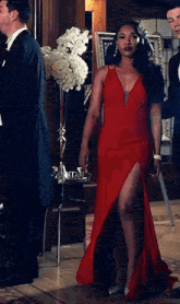 a woman in a red dress with a high slit is standing in a room with men .