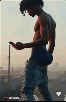 a man without a shirt is looking at his phone and has a heart next to his name