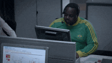 a man wearing a green and yellow adidas shirt is sitting in front of a computer monitor
