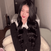 a girl with long black hair is sitting on a couch with a stuffed animal