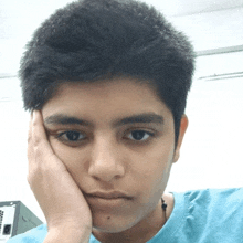 a young man in a blue shirt holds his hand to his chin
