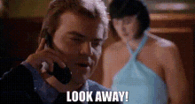 a man is talking on a cell phone while a woman in a blue dress stands behind him .